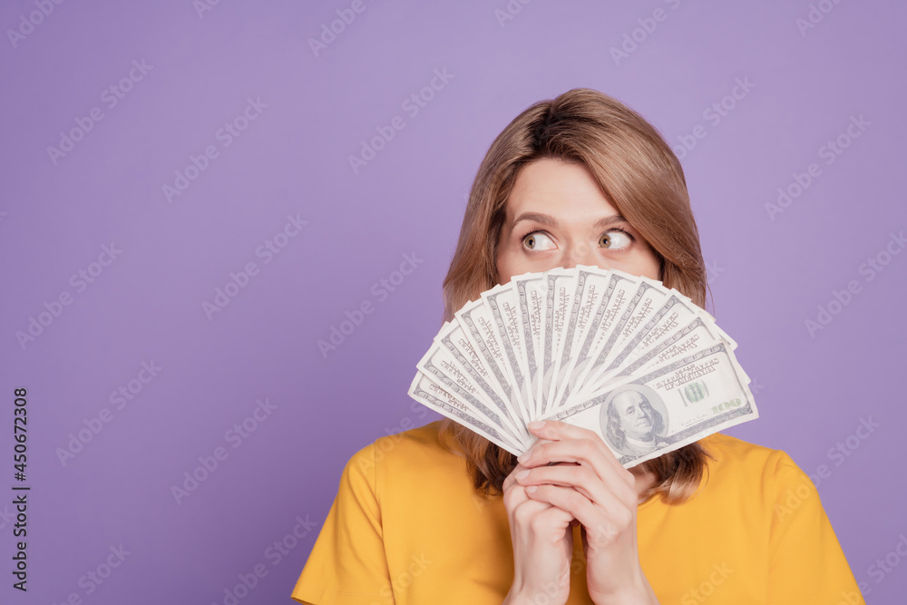 Photo of young pretty woman closing face bunch of dollars rich curious look empty space isolated over violet color background Photo of young pretty woman closing face bunch of dollars rich curious look empty space isolated over violet color background