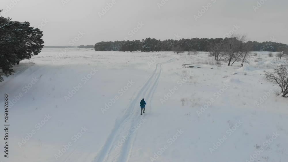 Aerial view of backpacker hiking snowy trail. Hiker with backpack walking on snowy road on cold winter day. A man walks through snow in the winter forest. Winter activity and recreation concept. Aerial view of backpacker hiking snowy trail. Hiker with backpack walking on snowy road on cold winter day. A man walks through snow in the winter forest. Winter activity and recreation concept.