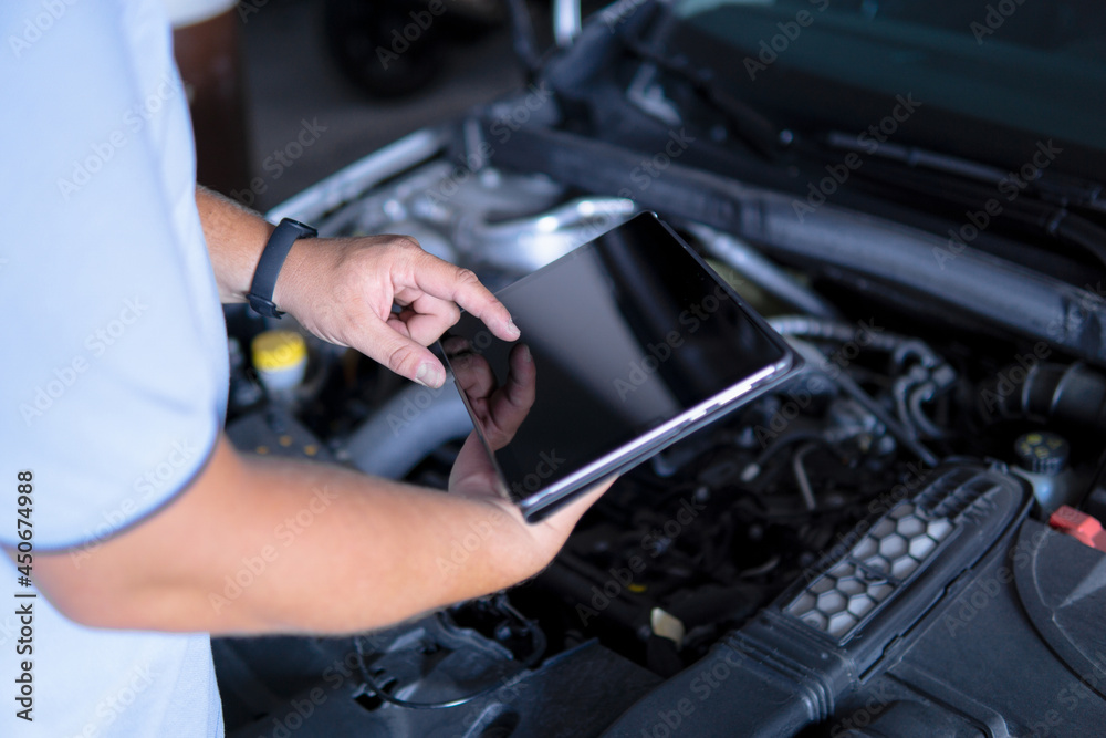 Auto mechanic with digital tablet at work making an engine repair diagnosis of a car in a mechanic garage