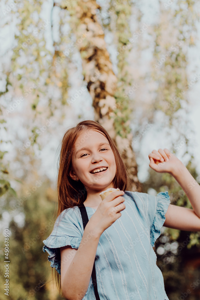 Little girl eating ice cream in summer park with green trees. Preteen walking outdoors enjoy sweet dessert Little girl eating ice cream in summer park with green trees. Preteen walking outdoors enjoy sweet dessert