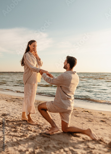 love and people concept - smiling young man with engagement ring making proposal to happy woman on beach