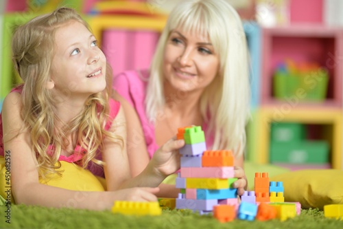  little daughter and mother playing with colorful plastic blocks at home