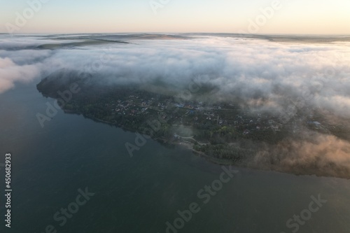 Aerial view of large river with fog above the water. Colorful landscape with forest in low clouds, river, meadow in fog, orange sky with sun in the morning. .Top view. Nature