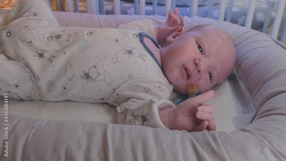 A newborn baby, one month old, cries in bed without a pacifier and