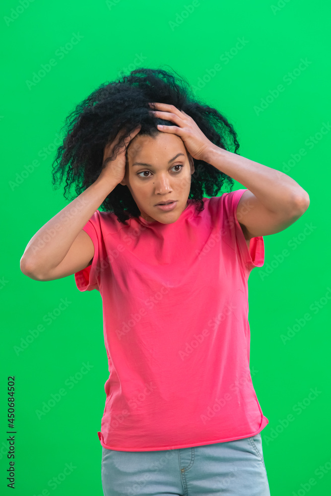 Portrait of young female African American angry and very upset. Black woman with curly hair in pink tshirt poses on green screen in the studio. Close up. Portrait of young female African American angry and very upset. Black woman with curly hair in pink tshirt poses on green screen in the studio. Close up.