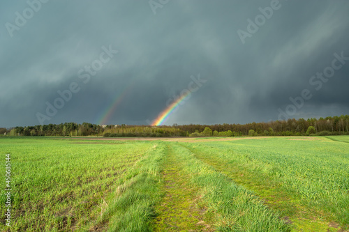 Cloudy sky with a fragment of a rainbow and a green meadow