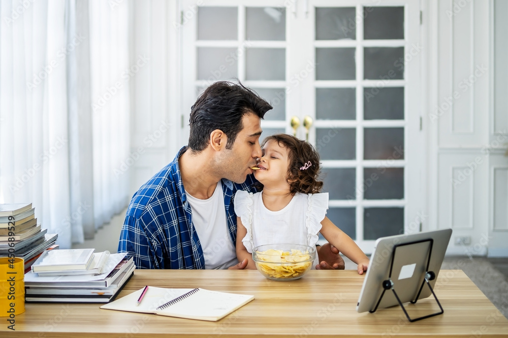 Caucasian family young father eating potato chips in mounth with little daughter together and watch cartoons educational online program Caucasian family young father eating potato chips in mounth with little daughter together and watch cartoons educational online program