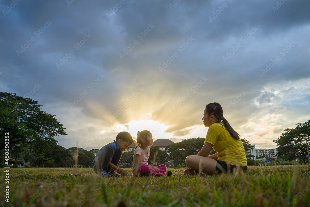 Mother and her kids playing on the green football field at the sunset time. Concept of friendly family.