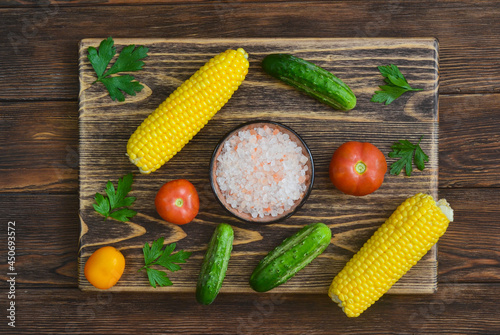 food background and ingredients for cooking summer salad, pink salt mineral, tomato, cucumber, corn, fresh vegetable on wooden table, vitamin for eating