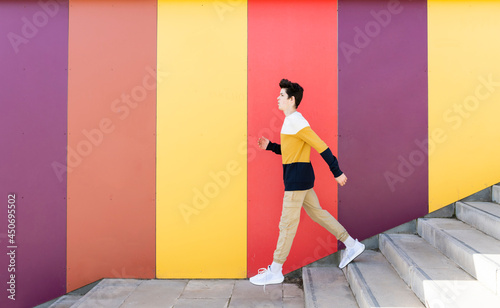 Adolescent going down stairs outdoor against colored wall photo