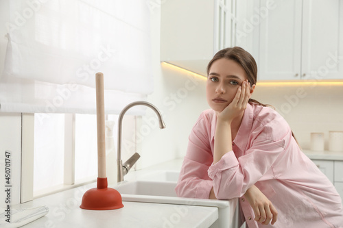 Canvastavla Unhappy young woman with plunger near clogged sink in kitchen