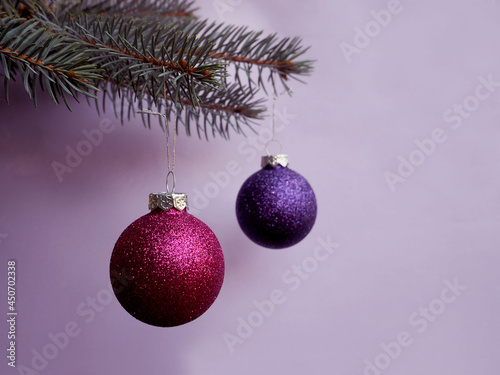 on the left, round pink and lilac Christmas shiny balls hang on a branch of the Christmas tree on a light purple background. copy space