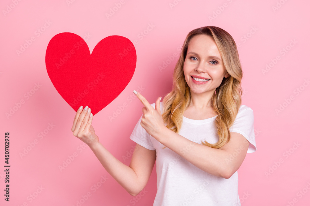 Photo of charming cute pretty mature woman point finger hold hand red paper heart isolated on pink color background Photo of charming cute pretty mature woman point finger hold hand red paper heart isolated on pink color background