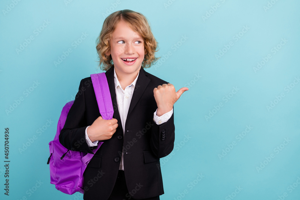Photo of excited curious kid direct finger empty space look side wear bag uniform isolated blue color background Photo of excited curious kid direct finger empty space look side wear bag uniform isolated blue color background