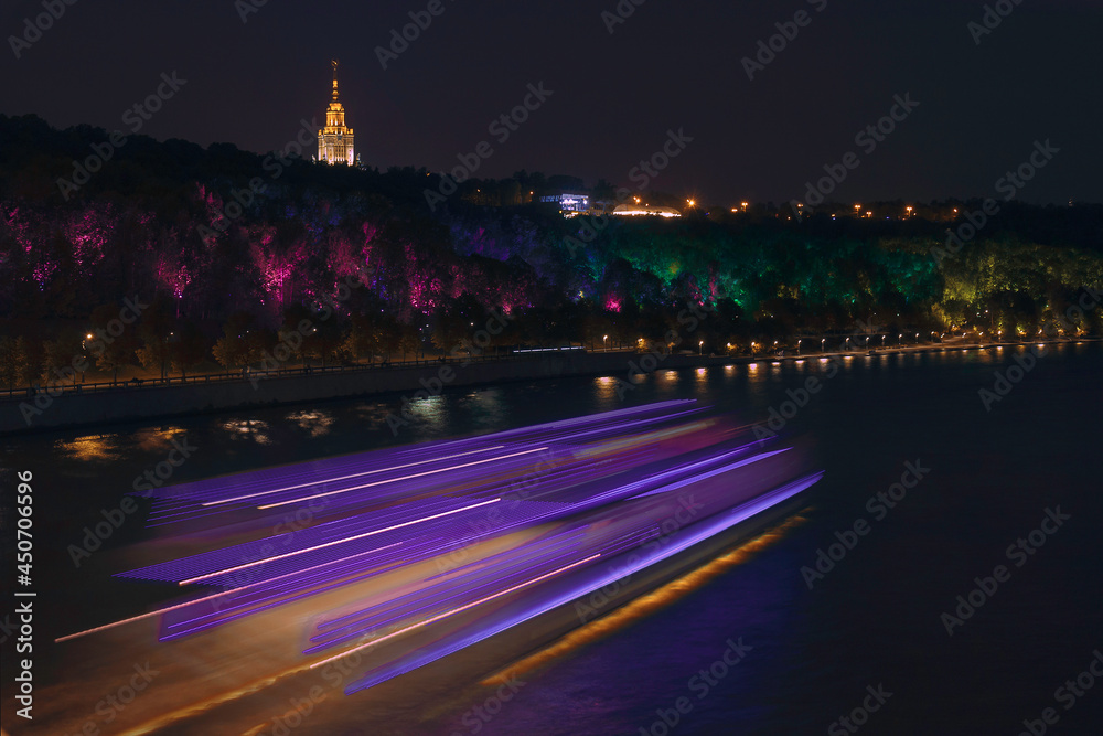 A spacey view of a night traffic on the river and colourful street light on an embankment. 