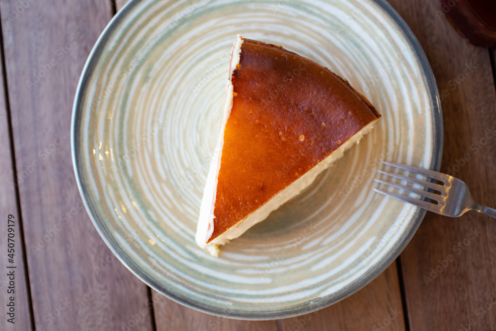 Fototapeta premium Cheescake San Sebastian slice on dish plate at cafe table.