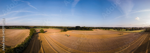 An aerial panoramic of the Suffolk countryside, a combine harvester is cutting and collecting grain while a tractor and trailer wait to collect the grain once the combine if full