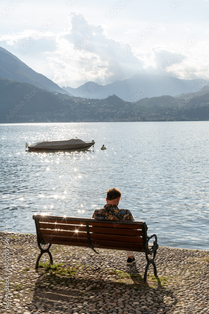 Personne assise sur un banc devant un paysage d'un lac et des montagnes en arrière plan 