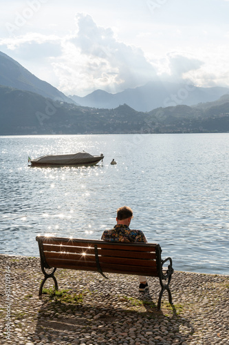 Personne assise sur un banc devant un paysage d'un lac et des montagnes en arrière plan 