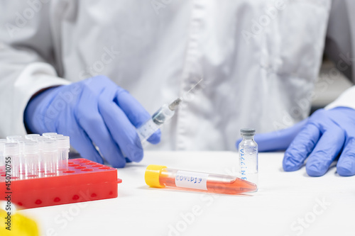 Medical tube with covid19 sign near bottle with vaccine and scientist with syringe on the background