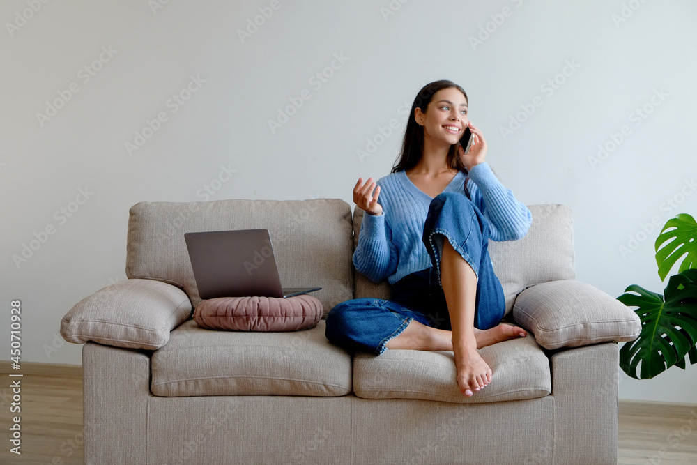 Joyful female having a fun video phone call. Portrait of young brunette woman wearing denim culottes, sitting on the couch texting and smiling. Background, copy space, close up. Joyful female having a fun video phone call. Portrait of young brunette woman wearing denim culottes, sitting on the couch texting and smiling. Background, copy space, close up.
