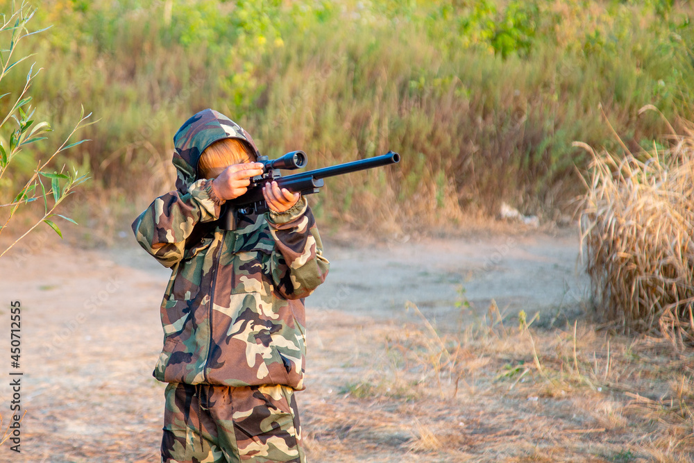 young hunter in a protective suit with a rifle getting ready to hit the target young hunter in a protective suit with a rifle getting ready to hit the target