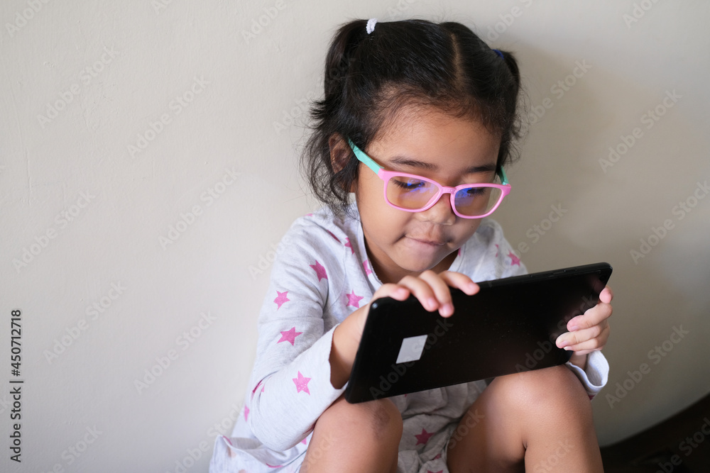 Asian little kid girl wearing anti radiation eye glasses while playing using mobile tablet device
