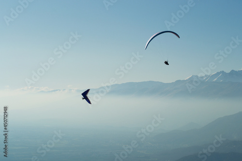 Paraglider and hang glider flying over the mountains in a hazy sky