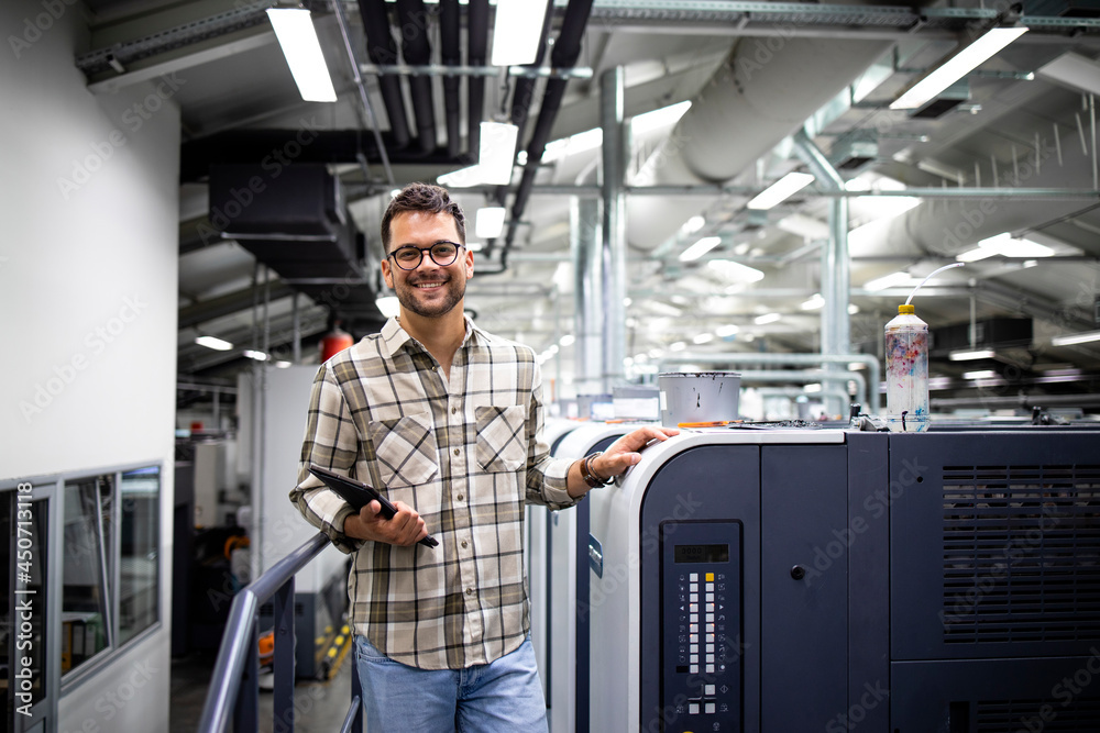 Portrait of print manager standing by large offset printing machine in print factory. Portrait of print manager standing by large offset printing machine in print factory.
