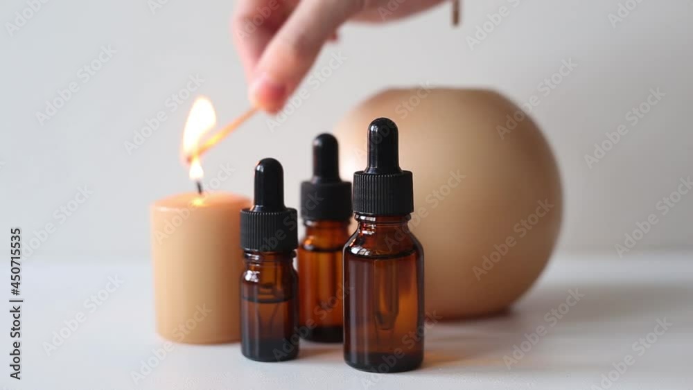 Brown glass bottles with serum, essential oil or other cosmetic product. A woman's hand lights candles. Natural organic cosmetic packaging, skin care and spa concept. Brown glass bottles with serum, essential oil or other cosmetic product. A woman's hand lights candles. Natural organic cosmetic packaging, skin care and spa concept.
