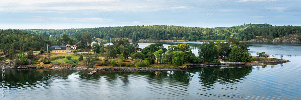 Amazing panoramic view of beautiful evergreens small islands and rocky coast of Scandinavia on sunny summer day. Shot from cruise ship. Forest green long coastline. Water voyage to Sweden Stockholm.