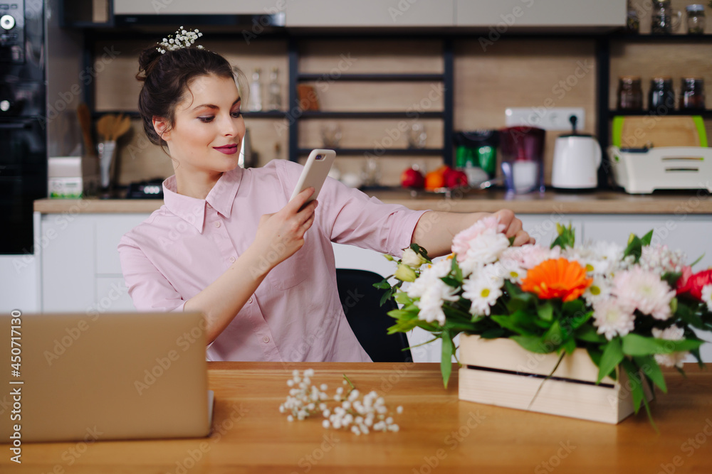 Smiling Woman Florist Small Business Flower Shop Owner. She is using her telephone and laptop to take orders for her online store. Take pictures Smiling Woman Florist Small Business Flower Shop Owner. She is using her telephone and laptop to take orders for her online store. Take pictures