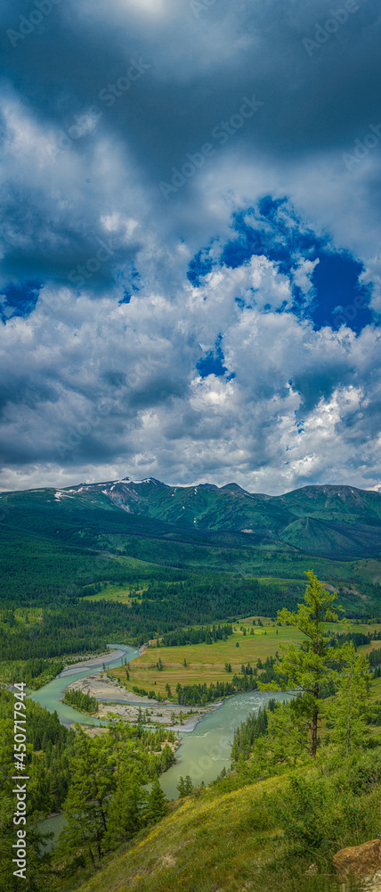 Obraz premium Panoramic view of plain with river near hills and mountains under white fluffy clouds in blue sky at sunny day