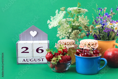 Calendar for August 26 : the name of the month of August in English, cubes with the number 26, bouquets of wild flowers, jars of jam, strawberries and cherries in cups, green background © MARYIA