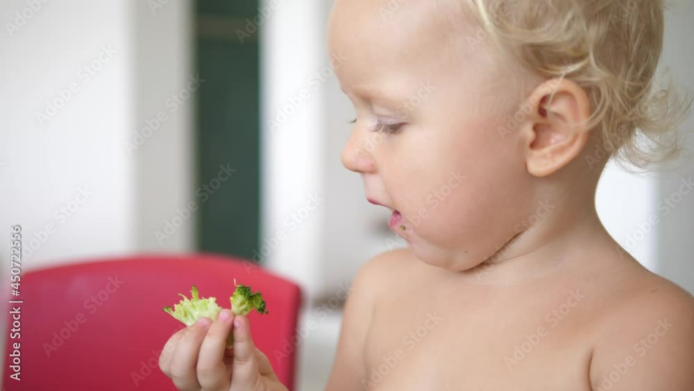 Close up of Caucasian toddler eating with great appetite healthy plant based snack of a broccoli. Healthy balanced diet for children Close up of Caucasian toddler eating with great appetite healthy plant based snack of a broccoli. Healthy balanced diet for children