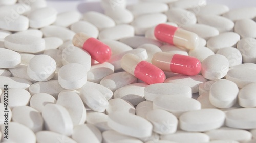 New bright pink and white capsules on the field of white tablets. A symbol of new medical technologies, new medicines of the modern pharmaceutical industry are superior to conventional medicines.