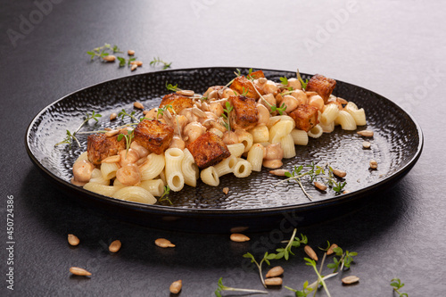 Delicious pasta with chickpeas, fried tofu and fresh herbs on black plate.