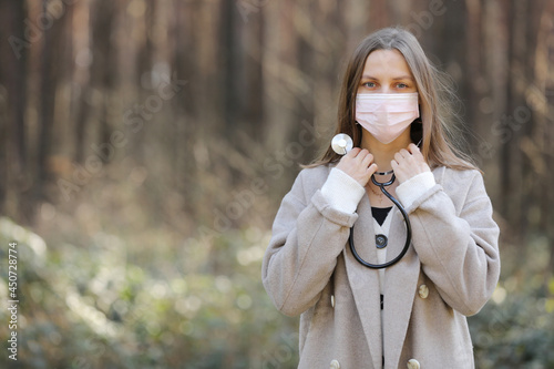 portrait of young woman in a face protective mask- girl with stethoscope around the neck-image of beautiful lady outdoors. copy space. © Andriy Medvediuk