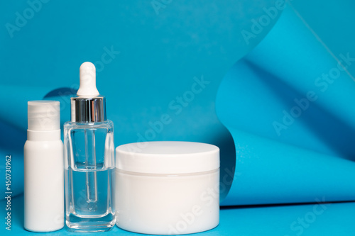 Art colourful geometry blue style and skin care cosmetics. Origami in a blue colour and cosmetics in white and blue colours: serum, face cream, face tonic. Paper mock up and luxury cosmetic. 