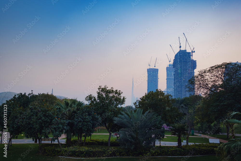 Alley with green lawn and trees in the Zabeel park, Dubai, UAE. View of the modern Dubai skyline from the approach highway to the Zabeel Palace, Dubai, United Arab Emirates