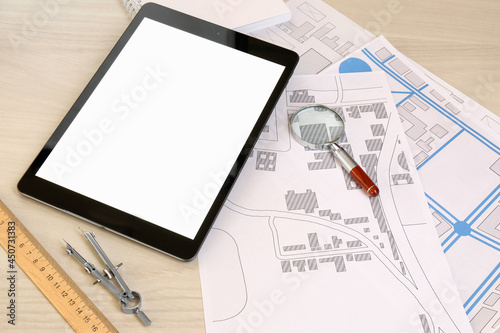 Office stationery, tablet and cadastral maps of territory with buildings on white wooden table
