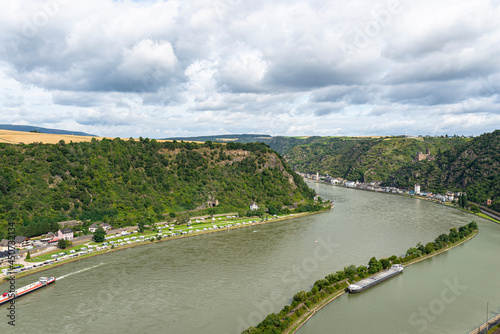 The river Rhine in western Germany flows between the hills covered with forest, visible barge and rock cliff.