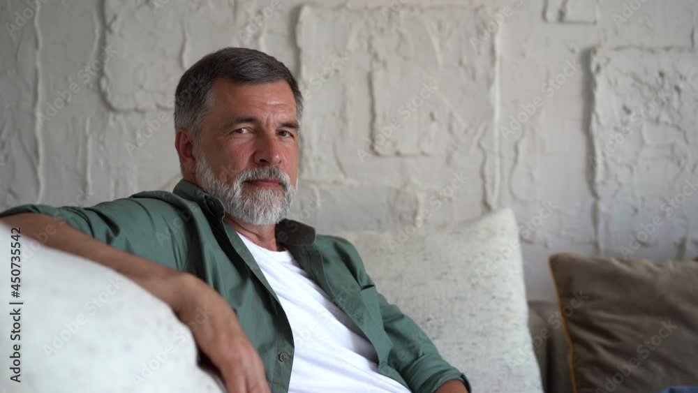 Smiling mature man relaxing on couch. Confident senior man with grey hair resting at home and looking at camera Smiling mature man relaxing on couch. Confident senior man with grey hair resting at home and looking at camera