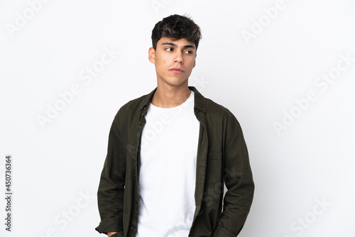 Young man over isolated white background having doubts while looking side