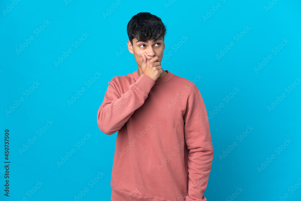 Young man over isolated blue background having doubts and with confuse face expression