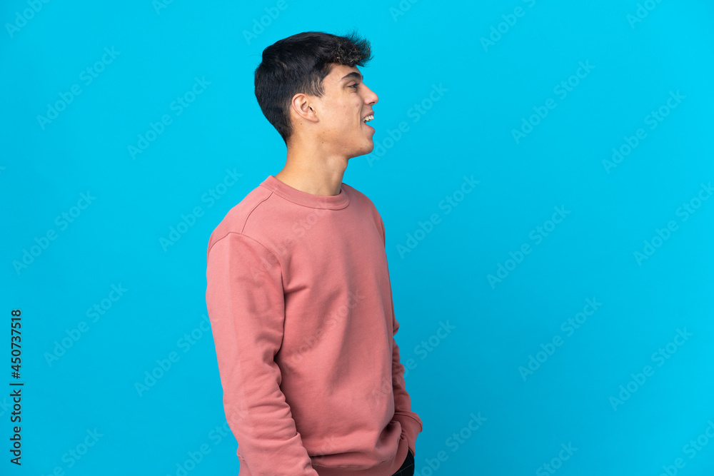 Young man over isolated blue background laughing in lateral position Young man over isolated blue background laughing in lateral position
