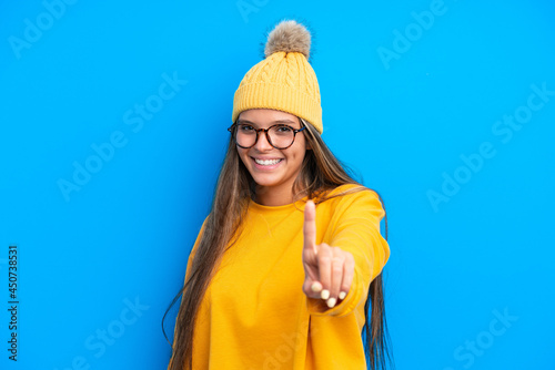 Young caucasian woman wearing winter clothes isolated on blue background showing and lifting a finger