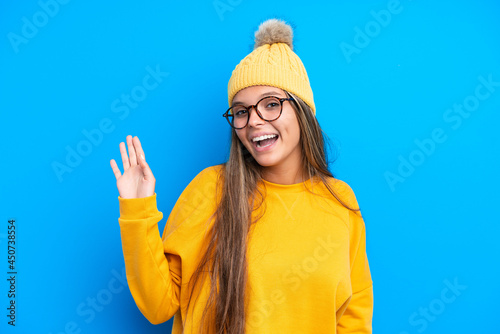 Young caucasian woman wearing winter clothes isolated on blue background saluting with hand with happy expression