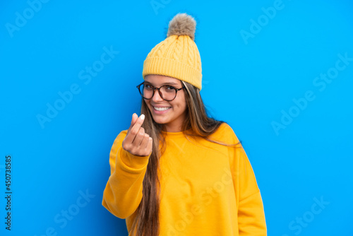 Young caucasian woman wearing winter clothes isolated on blue background making money gesture