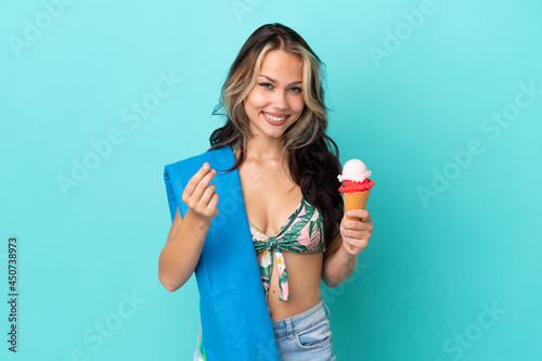 Teenager caucasian girl holding ice cream and towel isolated on blue background making money gesture